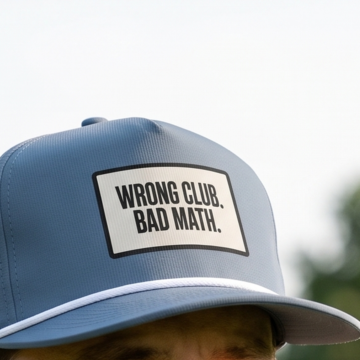 Close-up of the Wrong Club. Bad Math. rope hat in Blue Jean, worn outdoors. The bordered cream panel and black lettering are printed flat into the twill weave, above a white braided rope.