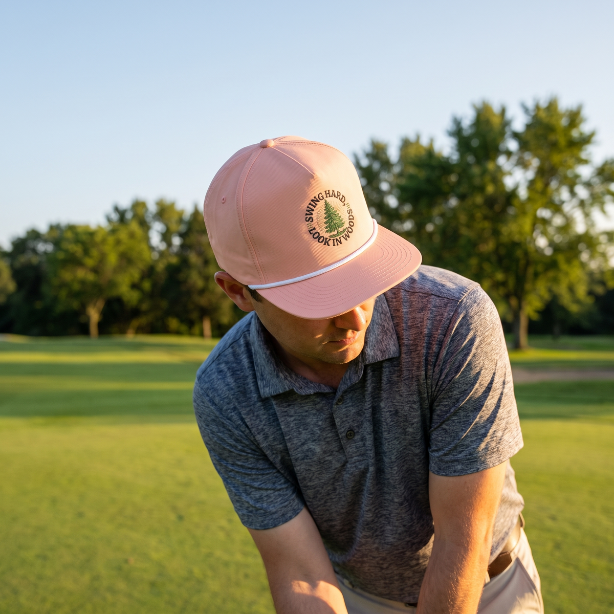 A golfer on a golf course wearing the Swing Hard, Look in Woods rope hat in Peachy with a white rope.