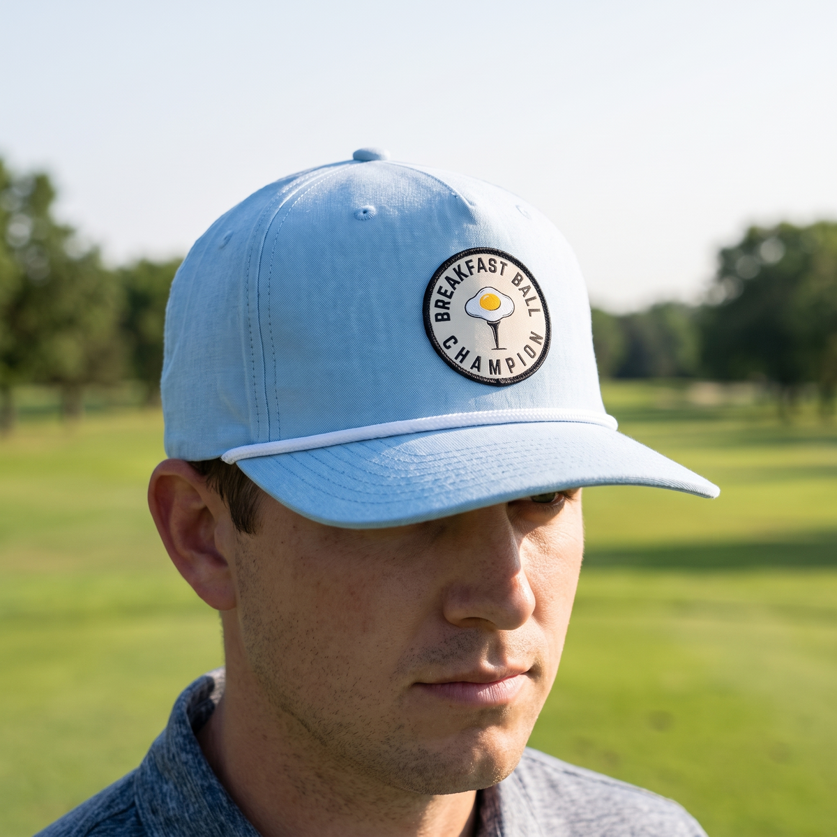 A golfer on a golf course wearing the Breakfast Ball Champion rope hat in Chambray with a white rope.
