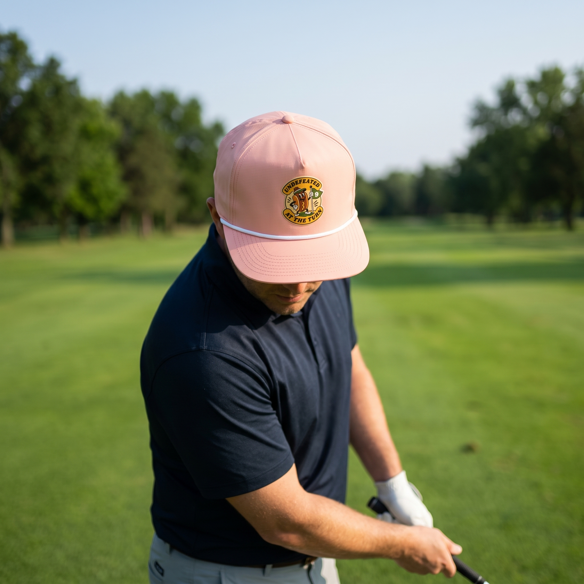 A golfer on a golf course wearing the Undefeated at the Turn rope hat in Peachy with a white rope.