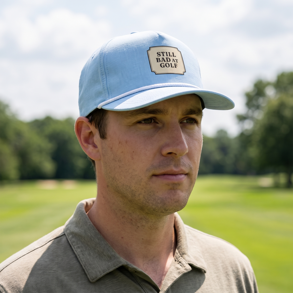 A golfer on a golf course wearing the Still Bad at Golf rope hat in Chambray with a white rope.