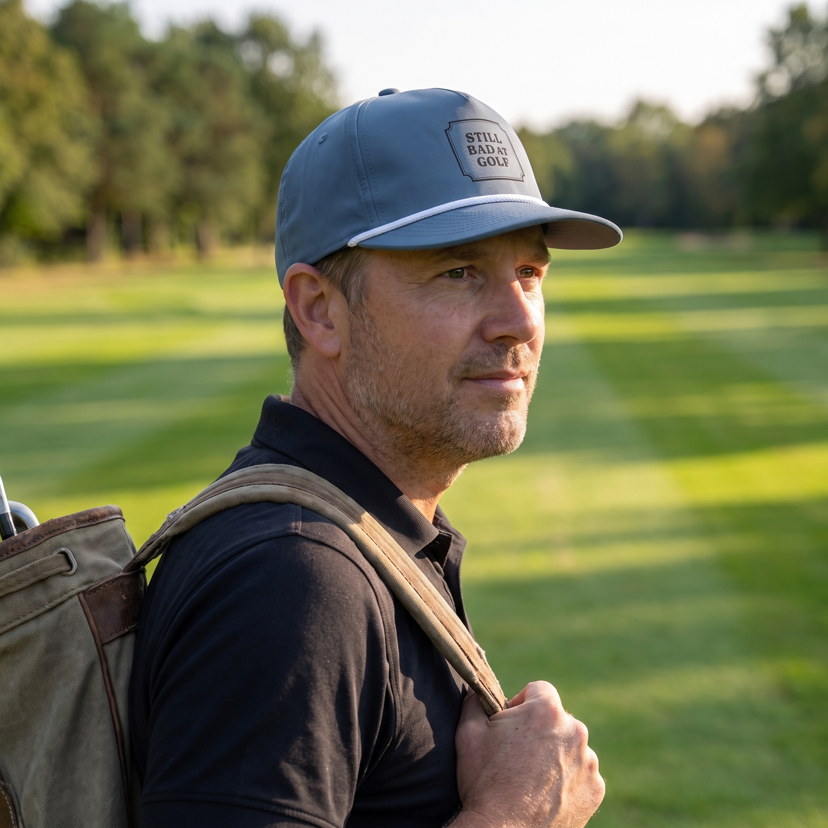 A golfer on the fairway in late afternoon light, golf bag on his shoulder, wearing the Still Bad at Golf rope hat in Blue Jean with a white rope.